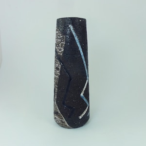 Peut inclure: Un vase cylindrique en céramique avec un extérieur brun foncé texturé. Le vase présente un motif linéaire en zigzag blanc et bleu clair. Le vase mesure environ 20 cm de haut.