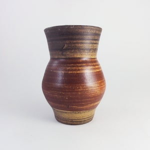 Può includere: Un vaso in ceramica fatto a mano con una superficie unica e strutturata. Il vaso presenta una calda tavolozza di colori, con fasce di marrone, beige e marrone rossiccio. Il design è di forma classica, adatto per esporre fiori o come elemento decorativo.