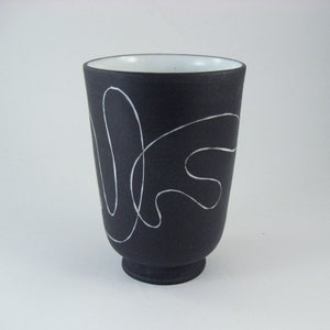 Może przedstawiać: Czarny ceramiczny wazon z białym abstrakcyjnym wzorem. Wazon ma szeroką podstawę i wąski otwór.