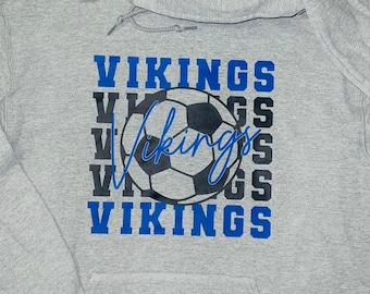 以下が含まれることがあります： 黒と白のサッカーボールのグラフィックと、青い文字で「VIKINGS」という単語が繰り返されているグレーのフード付きスウェットシャツです。