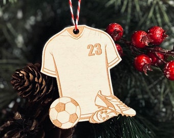 以下が含まれることがあります： サッカーのユニフォームの形をした木製クリスマスオーナメントで、前面に23の数字が書かれています。オーナメントにはサッカーボールとサッカーシューズのペアも付いています。