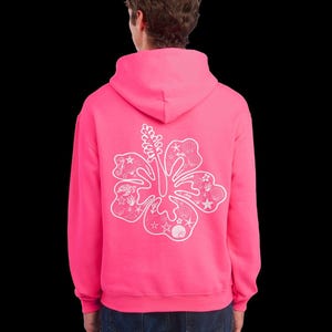May include: A bright pink hoodie featuring a white floral design on the back, with seashell and starfish details. The hoodie has a hood and long sleeves. The person is wearing blue jeans. The background is black.