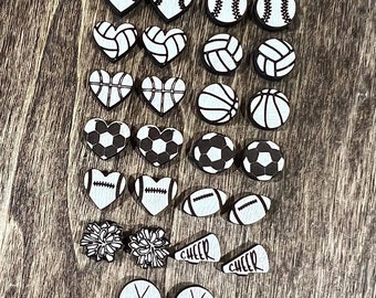 May include: A set of 20 white wooden earrings with various sports-themed designs, including baseballs, volleyballs, basketballs, soccer balls, footballs, hockey sticks, cheerleading megaphones, and pom-poms.