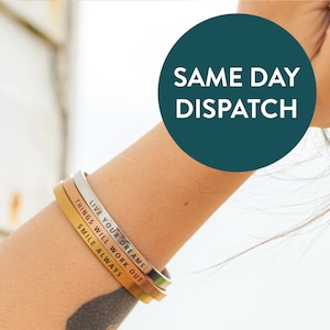 Puede incluir: Tres pulseras metálicas en plata, oro rosa y oro están apiladas en un brazo. Las pulseras tienen citas inspiradoras: "LIVE YOUR DREAMS", "THINGS WILL WORK OUT" y "SMILE ALWAYS". Un círculo turquesa con el texto "SAME DAY DISPATCH" está en el fondo.