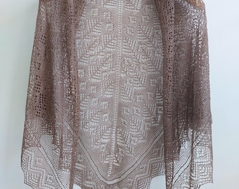 May include: A triangular shawl in a light brown colour featuring an intricate, openwork lace pattern. The design includes a central vertical spine with symmetrical geometric motifs and a decorative, pointed zigzag border along the bottom edge.