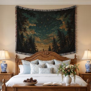 Puede incluir: Un tapiz de pared tejido rectangular que presenta un cielo nocturno oscuro lleno de estrellas sobre una silueta de pinos y nubes, acabado con un borde de flecos. La escena muestra tonos profundos de azul, verde y dorado cálido.
