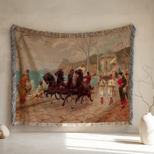 Op de afbeelding: Een geweven wandtapijt met een klassieke scène van een door paarden getrokken strijdwagen op een stenen pad bij de zee. Het kunstwerk toont donkere paarden die een wagen trekken met figuren in antieke kleding, omringd door architecturale elementen.