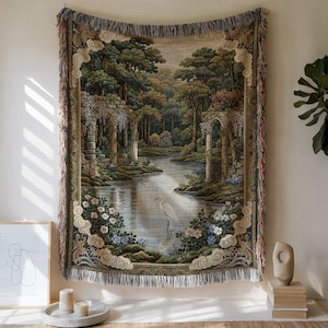 May include: A rectangular woven tapestry throw blanket featuring a detailed landscape scene with a white heron standing in a calm river, surrounded by stone ruins, lush green trees, and flowering bushes, finished with decorative fringed edges.