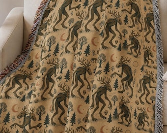 May include: A tan throw blanket featuring a repeating pattern of dark green, antlered creatures, trees, and crescent moons. The blanket has a fringed edge with brown, grey, and red hues. It is draped over a beige sofa.