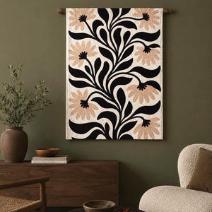 May include: A rectangular wall hanging featuring a cream-colored fabric base with a bold, repeating pattern of black curved leaves and stems interspersed with large, light tan flower blossoms, suspended from a dark wooden rod at the top.