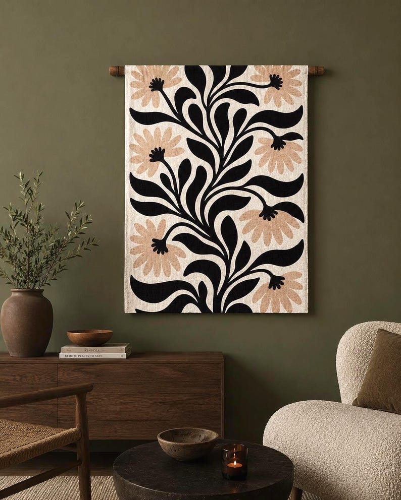 May include: A rectangular wall hanging featuring a cream-colored fabric base with a bold, repeating pattern of black curved leaves and stems interspersed with large, light tan flower blossoms, suspended from a dark wooden rod at the top.