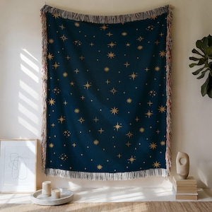 Peut inclure: Un plaid tissé bleu foncé orné d'un motif répétitif d'étoiles dorées de différentes tailles. La couverture présente une surface texturée et est finie avec des franges décoratives sur les bords supérieur et inférieur, offrant un aspect doux.