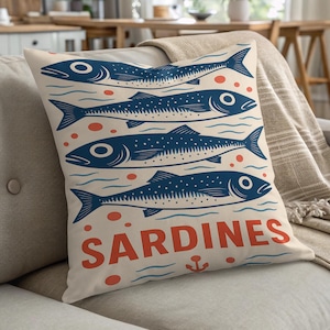 May include: A cushion with a cream background featuring a blue illustration of sardines. The design includes four fish, red dots, and the word "SARDINES" in red. An anchor is at the bottom.