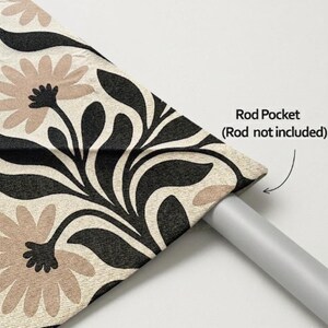 May include: A curtain panel featuring a cream-colored fabric with a repeating pattern of large, light brown flowers and bold black leaves. The top edge includes a rod pocket for hanging, with text indicating Rod Pocket (Rod not included).