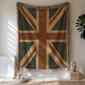 Pode incluir: Uma manta de tecido vintage com design de bandeira britânica, com bordas desfiadas. A manta apresenta um aspeto desgastado e desbotado com uma combinação de cores vermelho, branco e azul.
