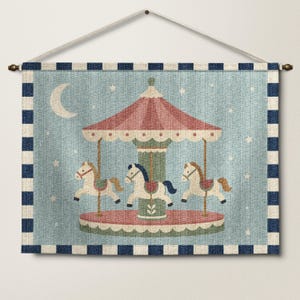 May include: A rectangular wall hanging featuring a carousel with three white horses on a light blue background with a crescent moon and stars. The carousel has a red roof and a green center pole. The border is a navy blue and white checkered pattern.