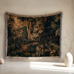 May include: A rectangular woven throw blanket featuring a detailed forest landscape scene with dense trees, lush foliage, and earthy tones of dark green, brown, and gold. The blanket has a decorative fringed edge along the top and bottom borders.