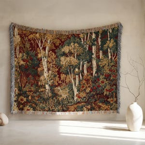 May include: A rectangular woven tapestry blanket featuring a detailed forest scene with tall birch trees, dense green foliage, and clusters of red berries against a deep burgundy background, finished with a decorative fringed edge on all sides.