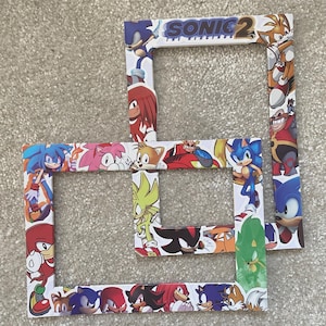 May include: Three white picture frames decorated with characters from the Sonic the Hedgehog franchise. The frames feature Sonic, Tails, Knuckles, and other characters. The top frame has the text "SONIC 2 THE HEDGEHOG".