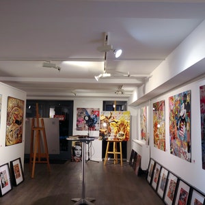 Pu&ograve; includere: Uno spazio di galleria con pareti bianche che espongono una variet&agrave; di opere d'arte colorate. Le opere d'art includono un'auto rossa, una mucca, un personaggio di Topolino e il viso di una donna. Ci sono anche diversi pezzi di arte incorniciati pi&ugrave; piccoli sulle pareti.