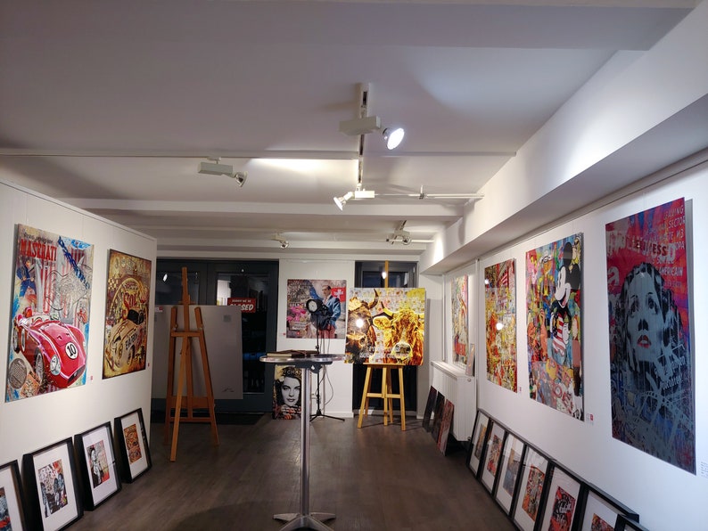Pu&ograve; includere: Uno spazio di galleria con pareti bianche che espongono una variet&agrave; di opere d'arte colorate. Le opere d'art includono un'auto rossa, una mucca, un personaggio di Topolino e il viso di una donna. Ci sono anche diversi pezzi di arte incorniciati pi&ugrave; piccoli sulle pareti.