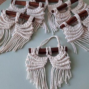 Pu&ograve; includere: Un set di sei arazzi da parete in macram&eacute; con accenti di bastoncino di cannella. Ogni arazzo presenta un motivo geometrico con dettagli a frangia.