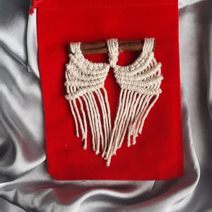 Pu&ograve; includere: Un paio di orecchini in macram&eacute; bianco con perni in legno, presentati su una pochette in velluto rosso.