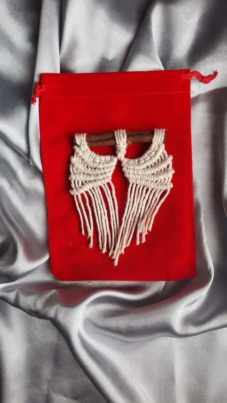 Pu&ograve; includere: Un paio di orecchini in macram&eacute; bianco con perni in legno, presentati su una pochette in velluto rosso.