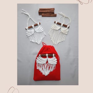 Pu&ograve; includere: Tre arazzi macram&eacute; bianchi con bastoncini di cannella, due sono su una superficie bianca e uno &egrave; su una pochette di velluto rosso.