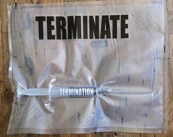 May include: A clear plastic package with the word "TERMINATE" in bold black letters. Inside, a syringe with the word "TERMINATION" is visible. The package is sealed and rests on a wooden surface.