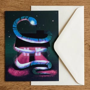 May include: A rectangular greeting card featuring a digital illustration of a glowing blue and purple snake coiled around a dark house silhouette against a starry night sky, accompanied by a plain white envelope for mailing and correspondence.