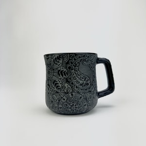 May include: A black ceramic mug with an intricate embossed floral design.