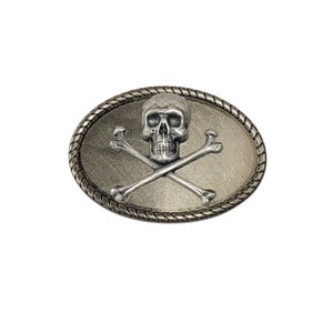 May include: Silver skull and crossbones belt buckle with a rope-like border. The buckle is oval shaped and has a brushed silver finish.