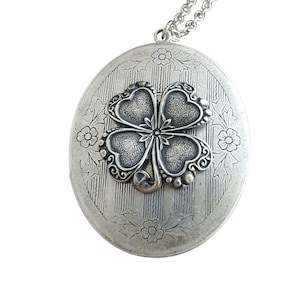 May include: Silver locket necklace with a four-leaf clover charm. The locket has an ornate design with a textured finish.