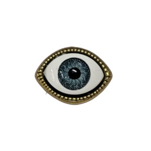 May include: A gold-rimmed evil eye charm with a blue iris and black pupil.
