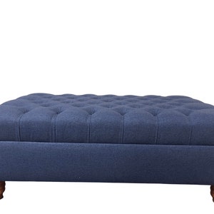May include: A navy blue tufted ottoman with wooden legs. The ottoman has a rectangular shape and a storage compartment.