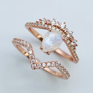 May include: Two gold rings set with clear stones. The top ring features a larger, pear-shaped stone in the centre and smaller stones around it. The bottom ring has a chevron shape with smaller stones.