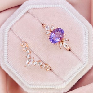 May include: A set of two delicate rose gold rings featuring a purple gemstone and clear cubic zirconia stones. The rings are presented in a pink velvet ring box.