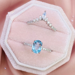 May include: Two silver rings with clear and blue gemstones. The top ring has a crown design with clear gemstones. The bottom ring has a blue oval gemstone surrounded by clear gemstones.