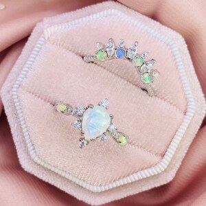 May include: Two silver rings with opal and diamond accents. The top ring is a delicate band with a row of opals and diamonds. The bottom ring features a large pear-shaped opal surrounded by smaller diamonds.
