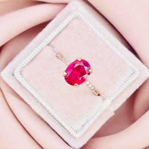May include: A red oval gemstone ring with a diamond band set in a white velvet ring box.
