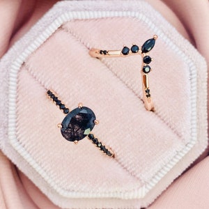 May include: Two rose gold rings with black gemstones. One ring has an oval-cut black gemstone and a black gemstone band. The other is a curved band with black gemstones. The rings are in a pink velvet ring box.