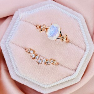 May include: Two gold rings set with white gemstones. The larger ring features a large oval-shaped gemstone and a delicate, twisted band. The smaller ring has a row of smaller gemstones.