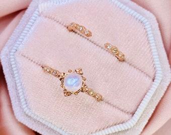 May include: Two gold rings with delicate designs. The larger ring features a round moonstone gemstone surrounded by a floral pattern. The smaller ring has a simple band with small diamonds.