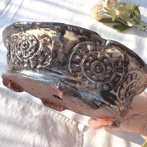 Può includere: Una ciotola in ceramica fatta a mano con finitura marrone scuro e lucida. La ciotola presenta disegni a spirale in rilievo sul bordo. La base è di colore marrone rossiccio. La ciotola è progettata per uso decorativo.