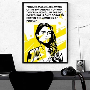Puede incluir: Impresión artística enmarcada en negro con un retrato estilizado de una mujer en blanco y amarillo. La impresión incluye una cita sobre el teatro y la memoria. Un escritorio negro con un portátil y una cámara en primer plano.
