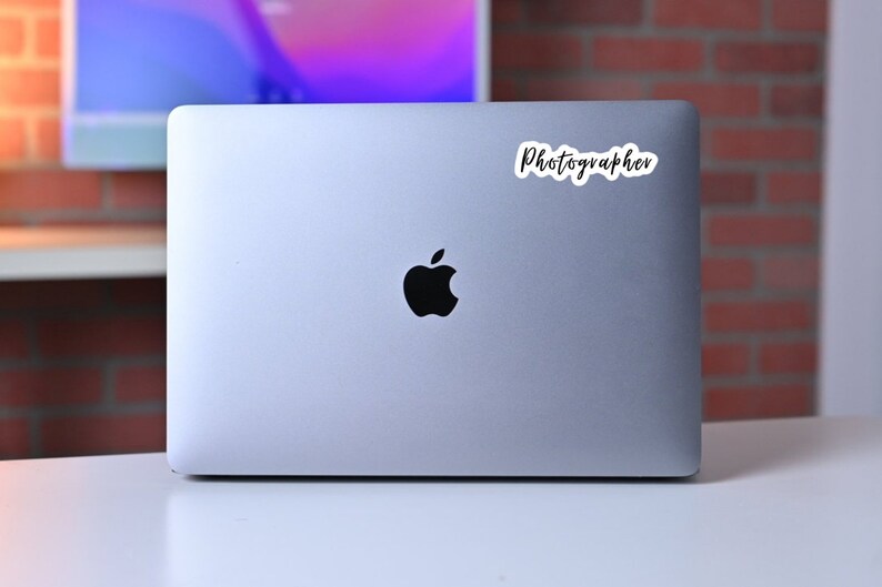 May include: A silver laptop computer with a black Apple logo and a white sticker that says "Photographer" on the top right corner.