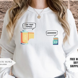 May include: White sweatshirt with a graphic of a film canister and a memory card with the text "I am your father" and "N0000000!" in speech bubbles.