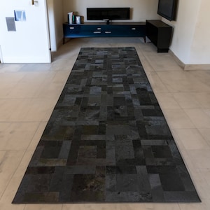 May include: A black and gray patchwork rug with a geometric pattern. The rug is made of leather and has a distressed look.