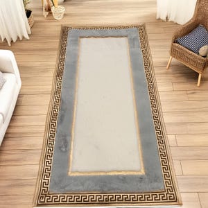 Pode incluir: Um tapete corredor cinza e bege com uma borda de chave grega. O tapete tem um centro cinza claro com uma borda bege.